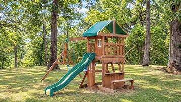 A wooden playground structure with a slide and swings in a grassy park area.