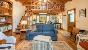 A spacious living room with a blue sofa, a wooden staircase, and a chandelier. - The Lil' Sipp, 2BR Cabin by Velvet Ditch Villas (Oxford)