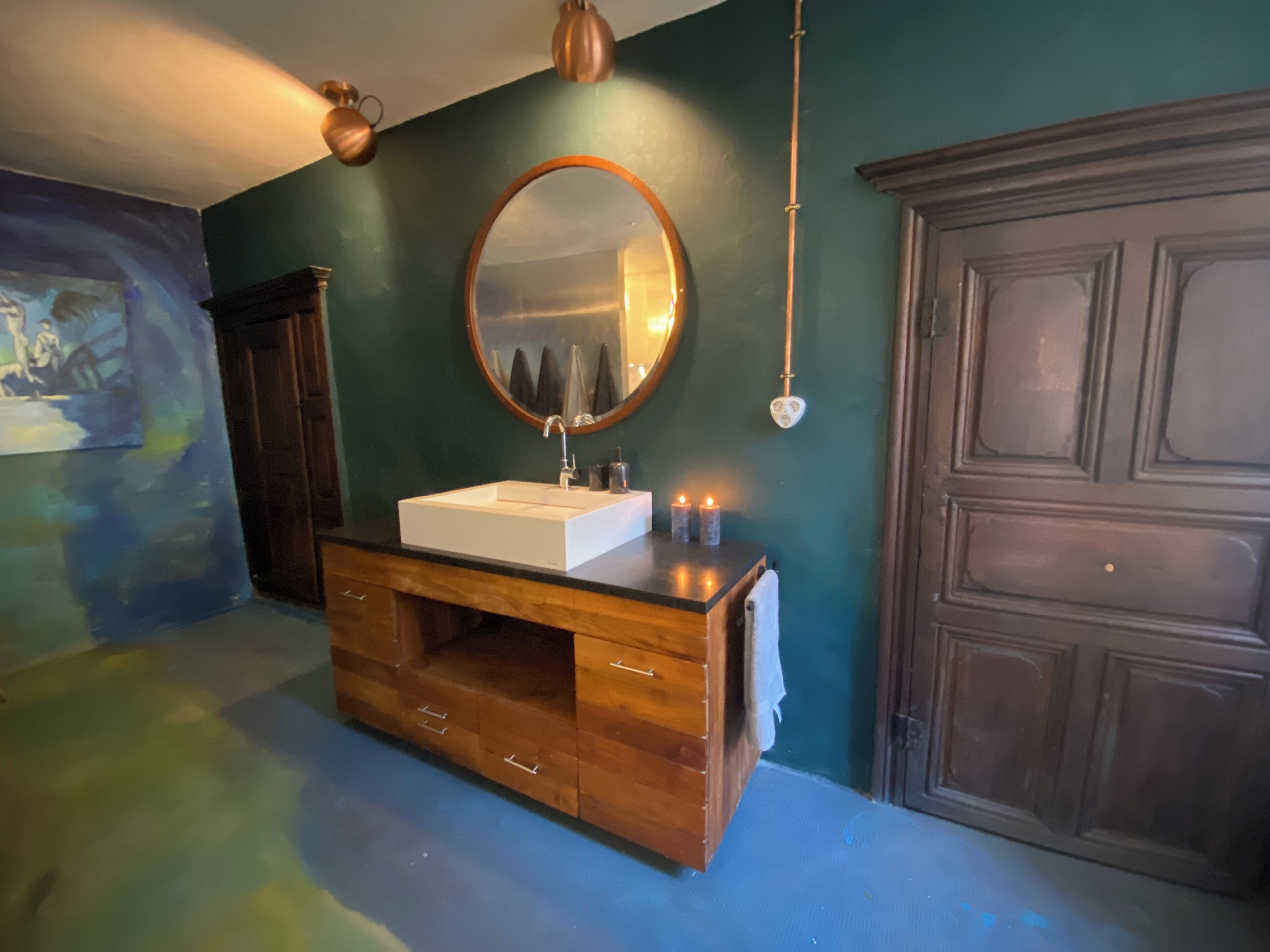 A bathroom with a wooden vanity, a round mirror, and a dark wooden cabinet.