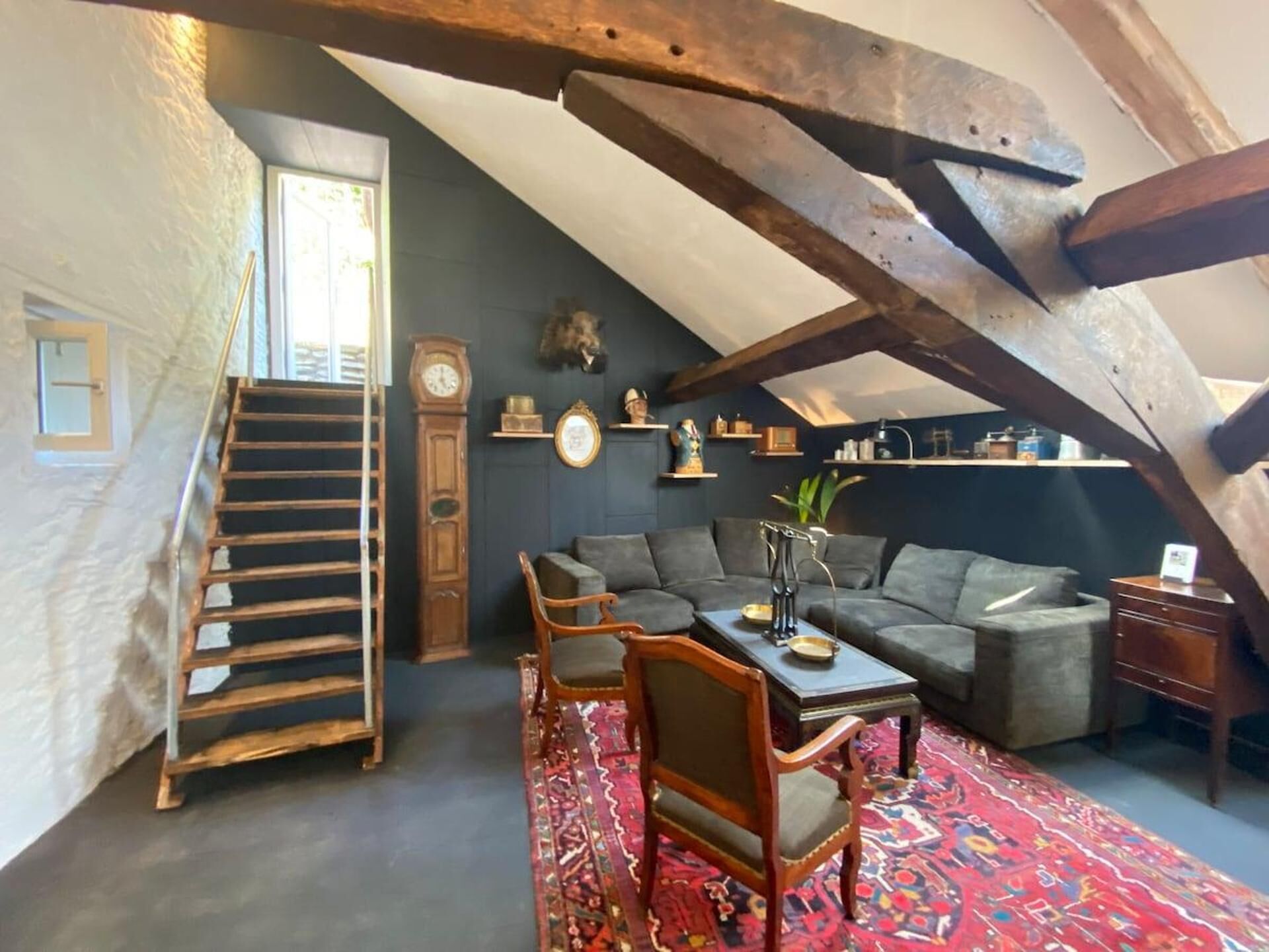An attic room with a staircase, a sofa, a coffee table, and a patterned rug.