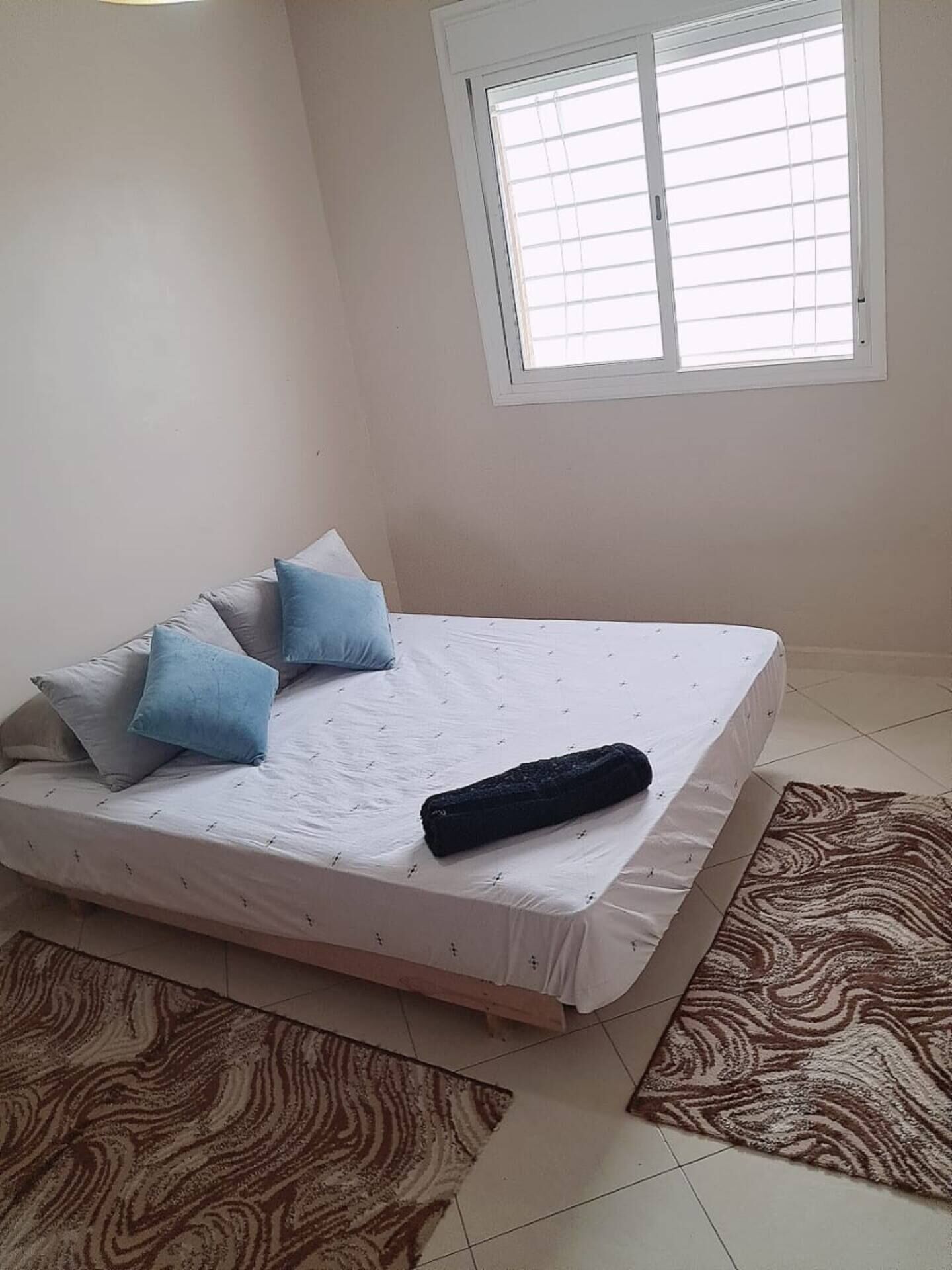 Une chambre à coucher avec un lit, des oreillers, une fenêtre et un tapis à motifs.