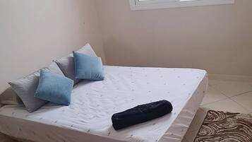 Une chambre à coucher avec un lit, des oreillers, une fenêtre et un tapis à motifs.