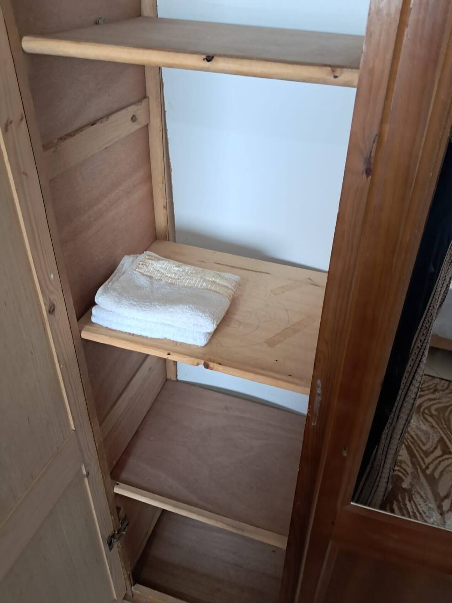 Un estante de madera con tres repisas, una de las cuales sostiene una toalla blanca doblada.