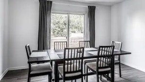 Uma sala de jantar com mesa e cadeiras, um ventilador de teto e uma janela com cortinas.