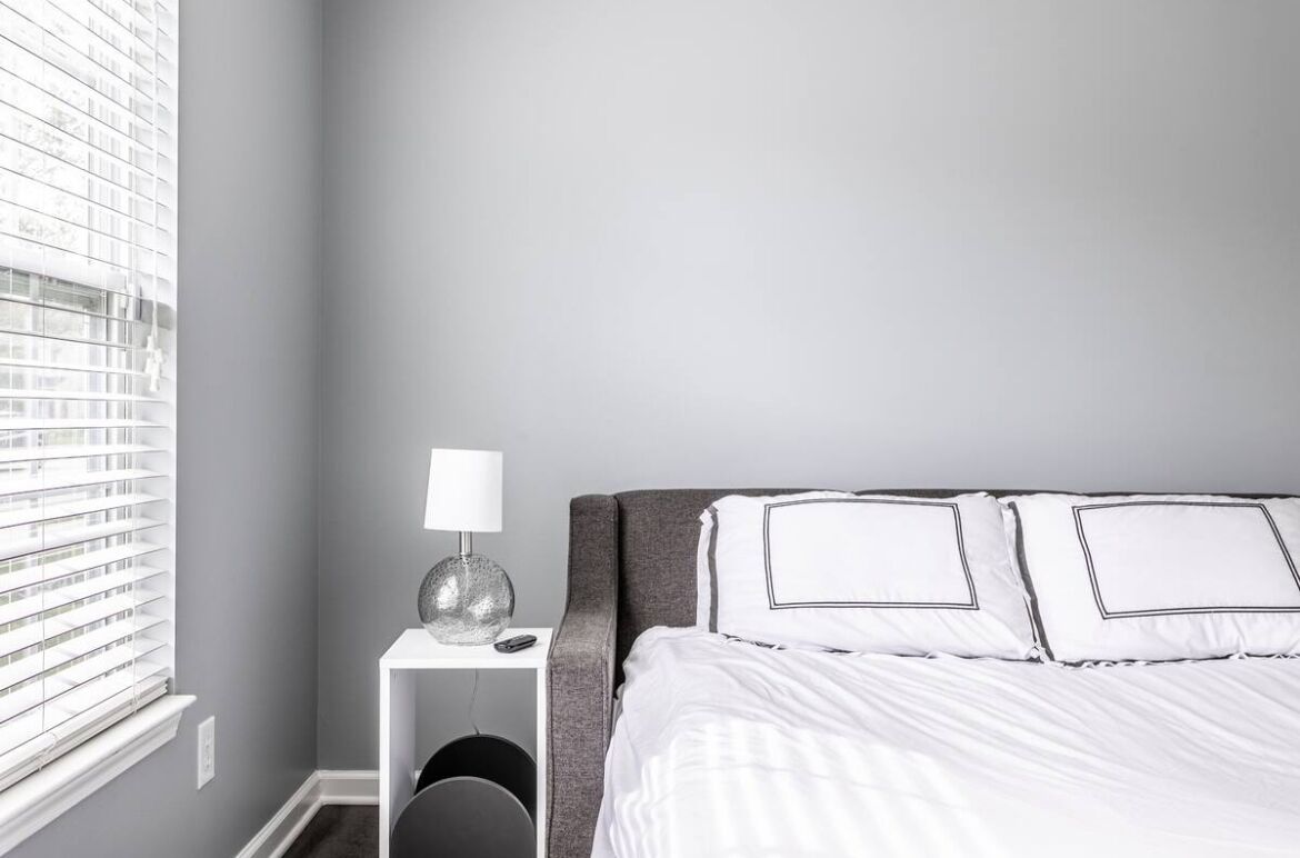Habitación de hotel ordenada con cama, mesita de noche con lámpara y ventana con persianas.