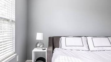Habitación de hotel ordenada con cama, mesita de noche con lámpara y ventana con persianas.