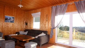 A wooden interior with a sofa, ottomans, a coffee table, and a large window with curtains. - Ferienhaus in Bansin am See (Heringsdorf)