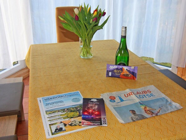 A table with a magazine, a chocolate bar, a bottle, and a vase with flowers. - Ferienhaus in Bansin am See (Heringsdorf)