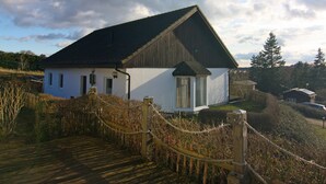 A white building with a dark roof, surrounded by a wooden fence and a rope barrier. - Ferienhaus in Bansin am See (Heringsdorf)