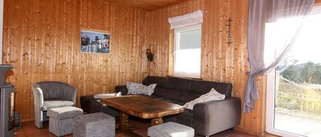 A cozy room with a wooden interior, a sofa, two armchairs, a coffee table, and a window with curtains.