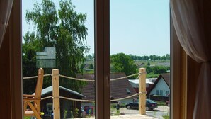 A view through a window of a wooden deck with a rope swing, a small building, and a car parked nearby. - Ferienhaus in Bansin am See (Heringsdorf)