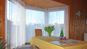 A wooden-paneled room with a table set for two, a chair, a vase with flowers, a bottle, and a menu. - Ferienhaus in Bansin am See (Heringsdorf)