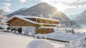 A wooden chalet with a sloped roof, surrounded by snow-covered trees and mountains, with a clear sky. - Holiday Home in Neukirchen With Mountain Views (Neukirchen am Grossvenediger)