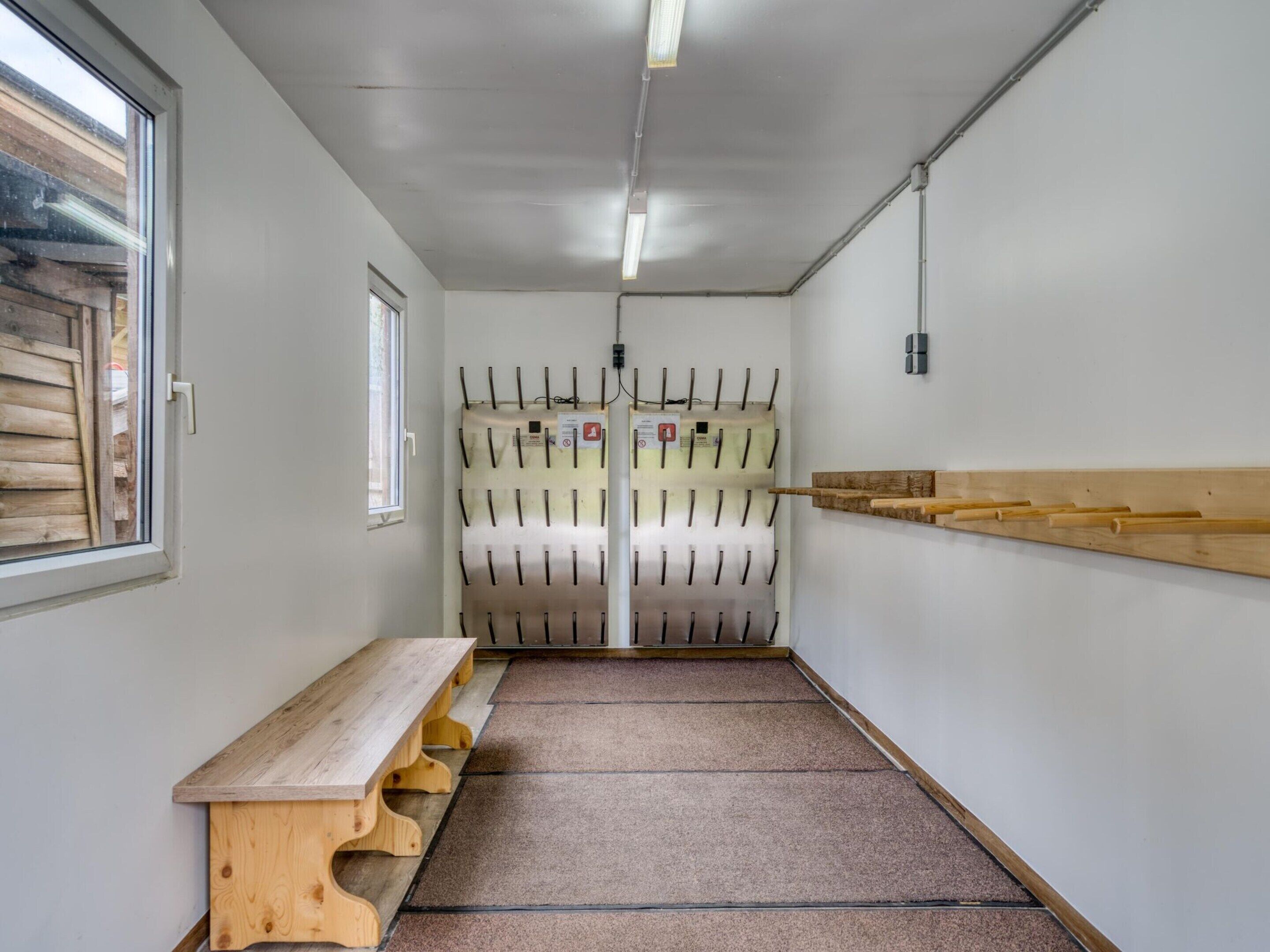 A narrow hallway with a wooden bench, a wall-mounted rack with hooks, and a window on the left.