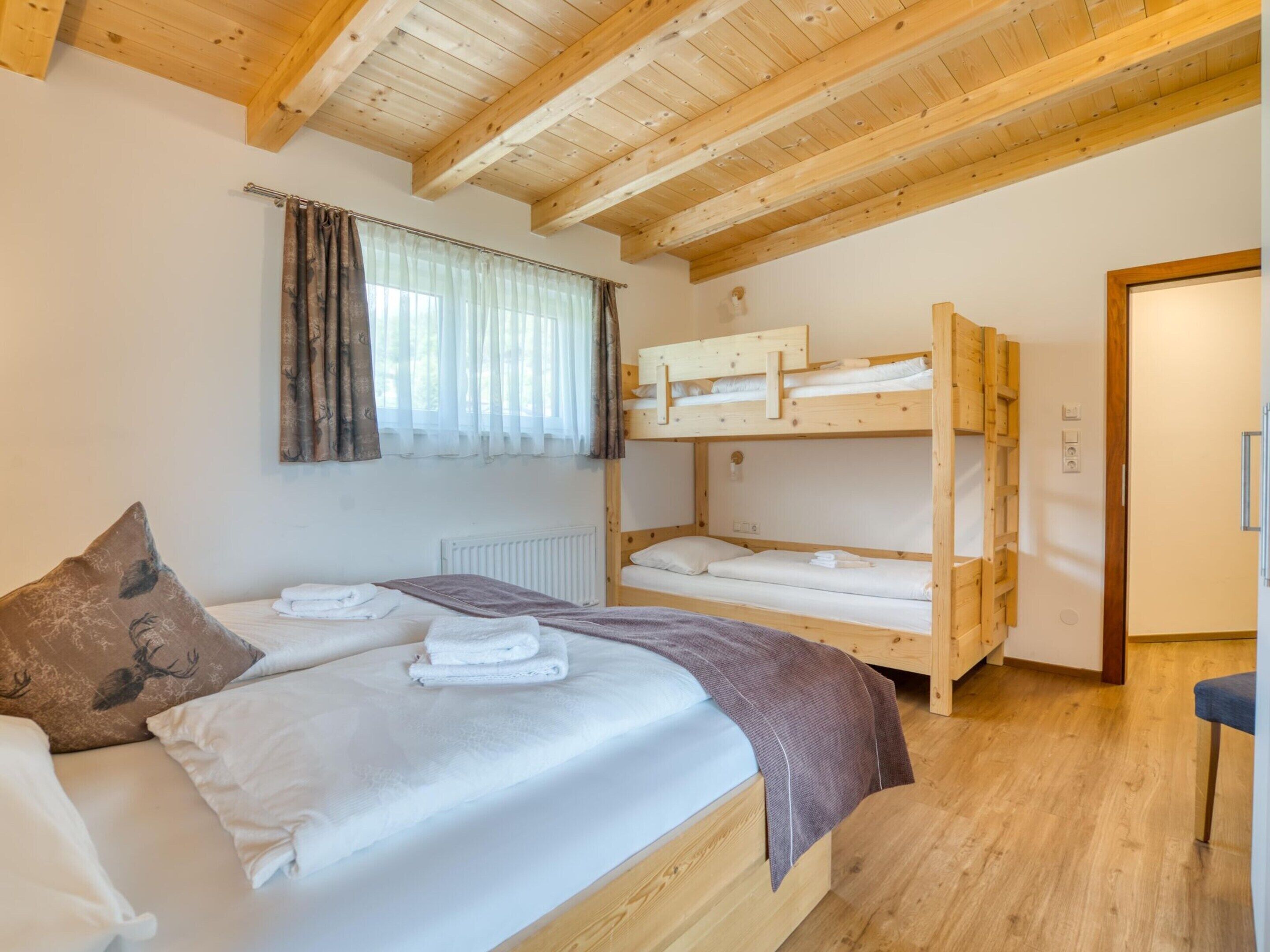 A room with a single bed, a bunk bed, wooden beams, a window with curtains, and a radiator.