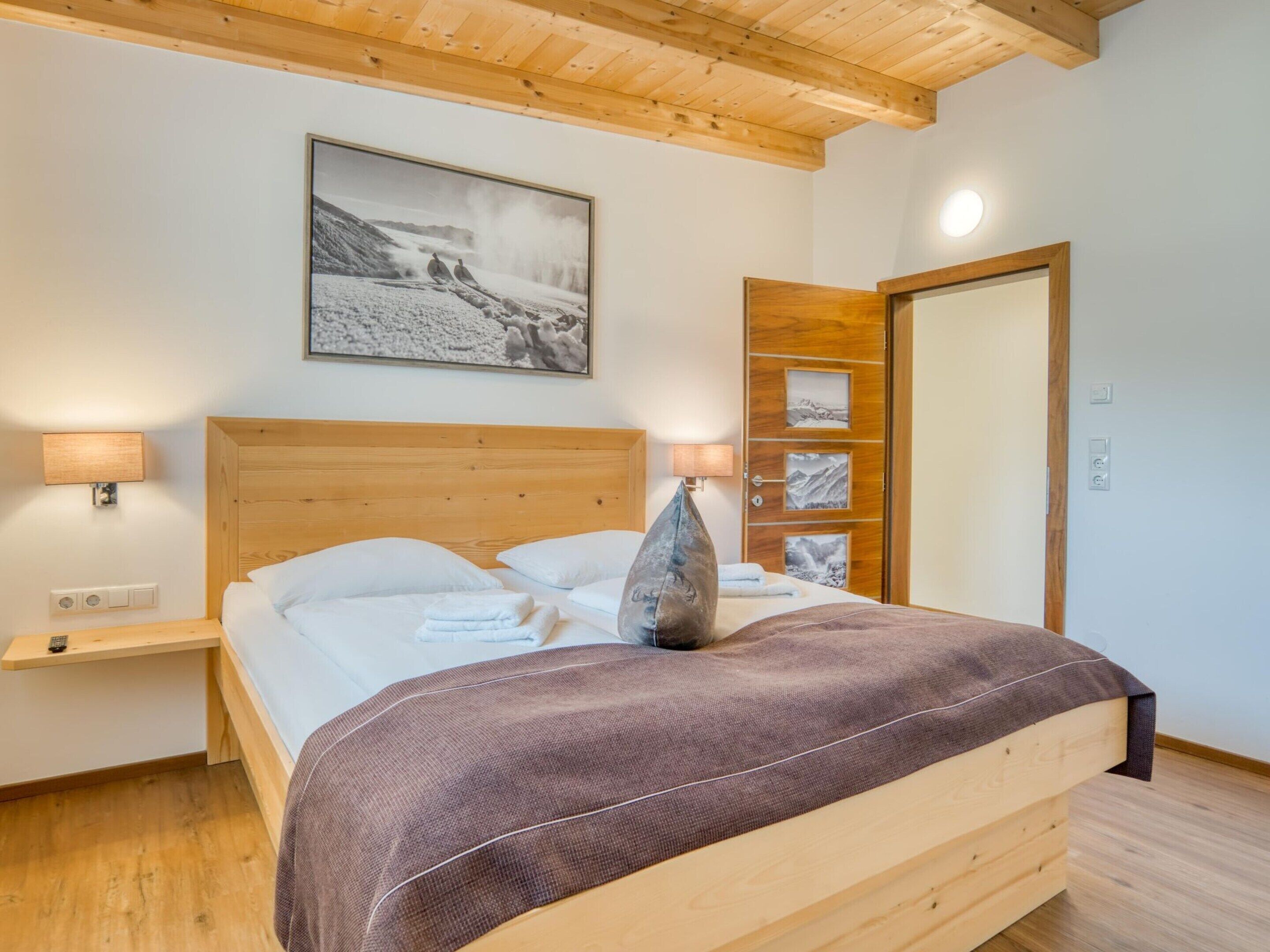 Une chambre à coucher avec un lit en bois, une table de chevet, une lampe fixée au mur et une porte ornée d’un cadre de photo.