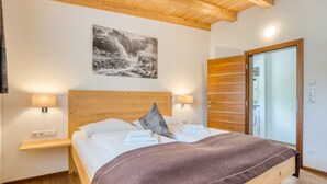 A bedroom with a wooden bed, two bedside lamps, a wooden headboard, a wall-mounted picture, and a wooden wardrobe. - Holiday Home in Neukirchen With Mountain Views (Neukirchen am Grossvenediger)