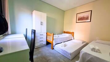 A small, clean room with two single beds, a wooden wardrobe, a desk with a chair, and a framed picture on the wall.