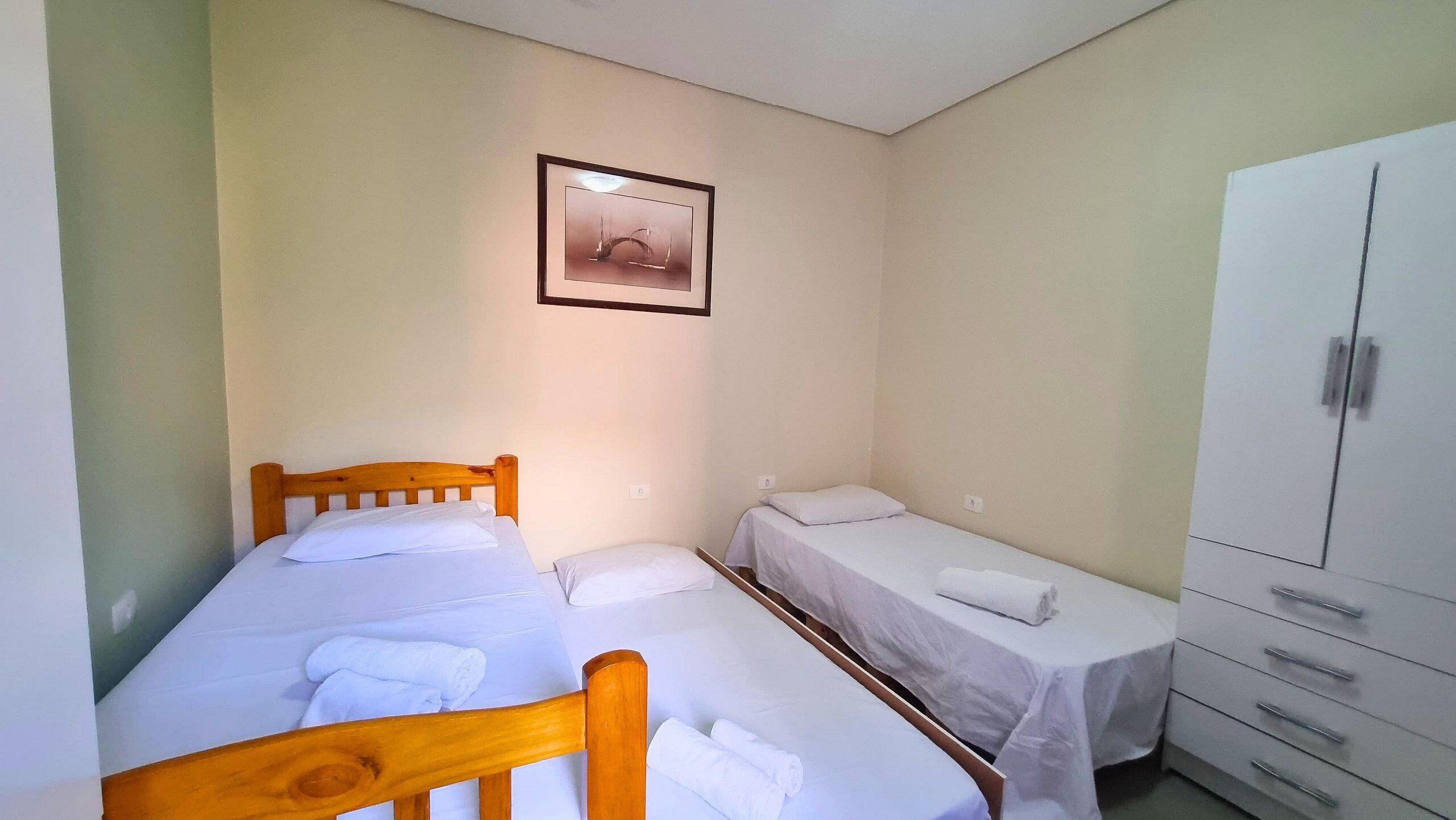 A room with two single beds, a wooden headboard, a wardrobe, and a framed picture on the wall.