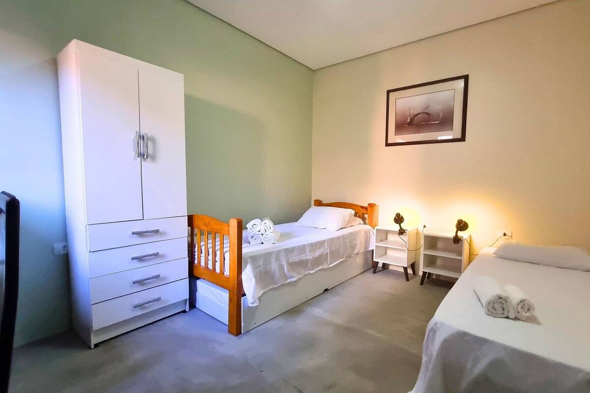 Ein kleines, sauberes Zimmer mit einem Einzelbett, einem Kleiderschrank, einem Schreibtisch und einem Nachttisch mit Lampen.