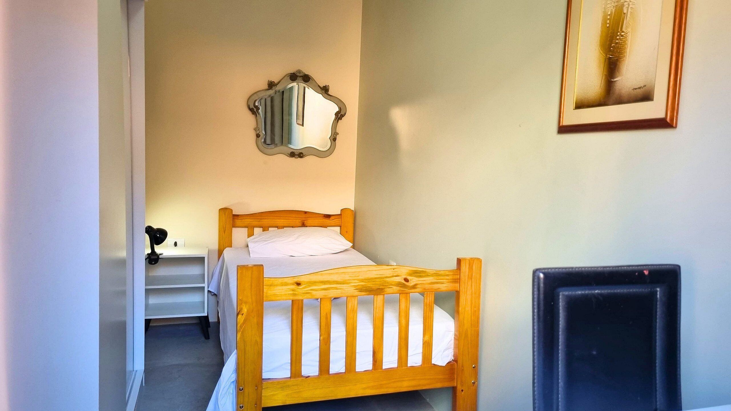 A bedroom with a wooden bed, a bedside table, a mirror, and a radiator.