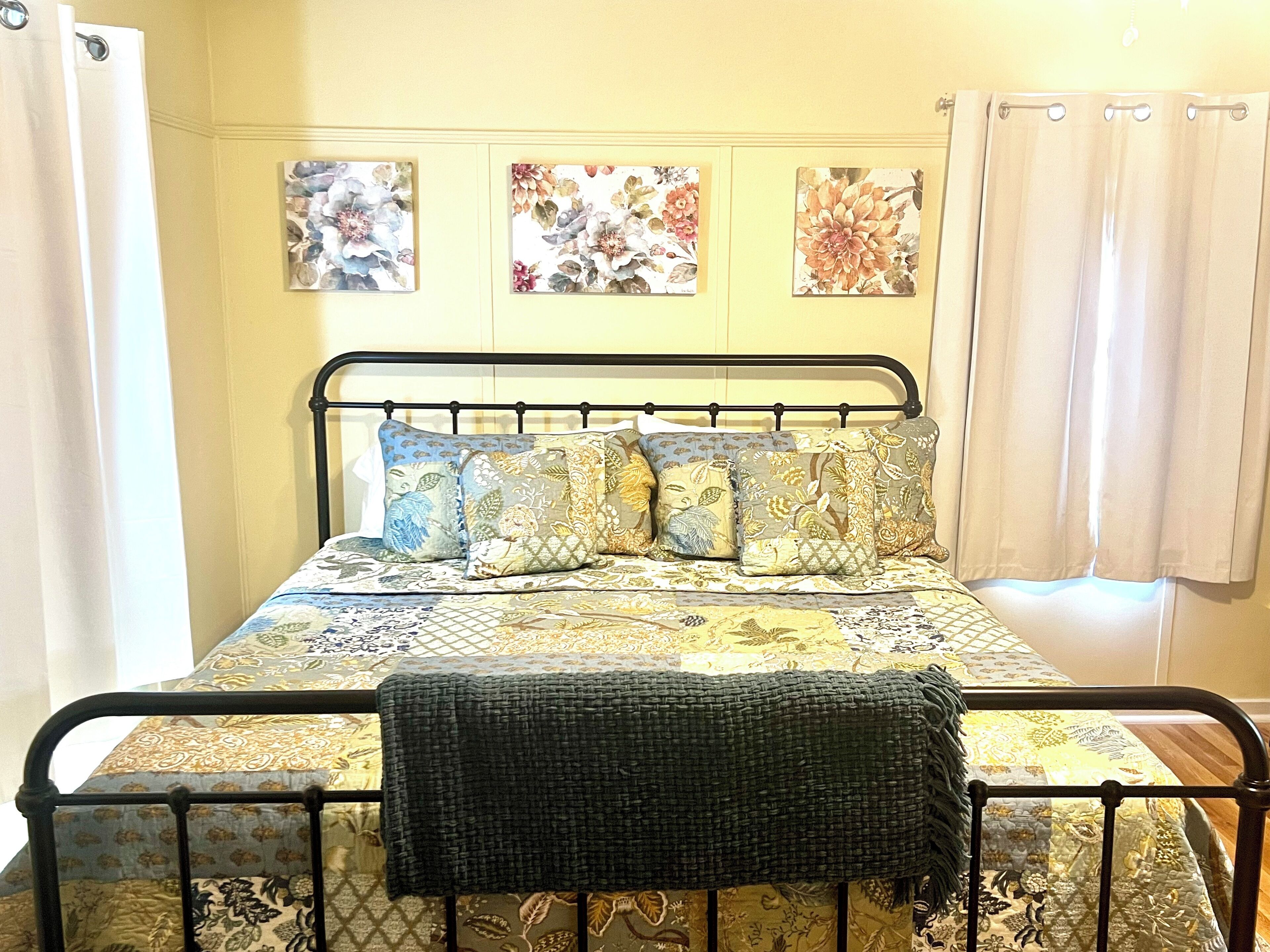 Cama com estrutura metálica, roupa de cama estampada com flores e manta escura.