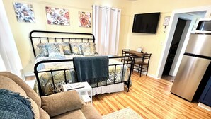 A cozy living room with a sofa, a small table, a ceiling fan, and a kitchen area with a refrigerator. - Historic Hilltop Guesthouse - Charming studio/cottage one block from downtown  (Laurel)