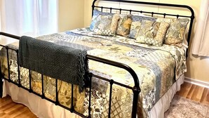 A bed with a metal frame, floral bedding, and a blanket. - Historic Hilltop Guesthouse - Charming studio/cottage one block from downtown  (Laurel)