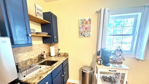 A kitchen with dark blue cabinets, a granite countertop, a stainless steel trash can, and a window with curtains. - Historic Hilltop Guesthouse - Charming studio/cottage one block from downtown  (Laurel)