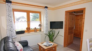 Una sala de estar con un sofá de cuero, una mesa de centro de madera, una planta en maceta, un televisor y una puerta de madera que da a otra habitación.