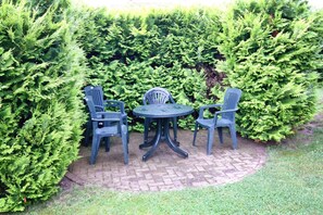 A patio with a round table and four chairs, surrounded by dense green hedges. - Einladende Ferienwohnung am Achterwasser in Lutow (Luetow)