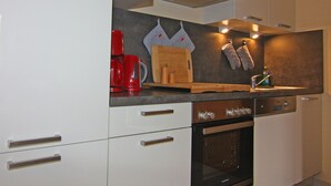 Una cocina moderna con armarios blancos, horno empotrado, cafetera roja y tabla de cortar de madera.