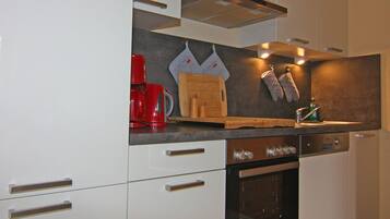 A modern kitchen with white cabinetry, a built-in oven, a red coffee maker, and a wooden cutting board.