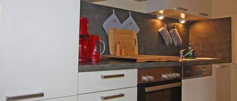 A modern kitchen with white cabinetry, a built-in oven, a red coffee maker, and a wooden cutting board.