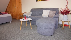 Una sala de estar con un sofá gris, una mesita redonda con una vela roja, un armario de madera y un cuadro en la pared.