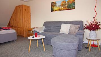 A living room with a grey sofa, a small round table with a red candle, a wooden cabinet, and a painting on the wall.