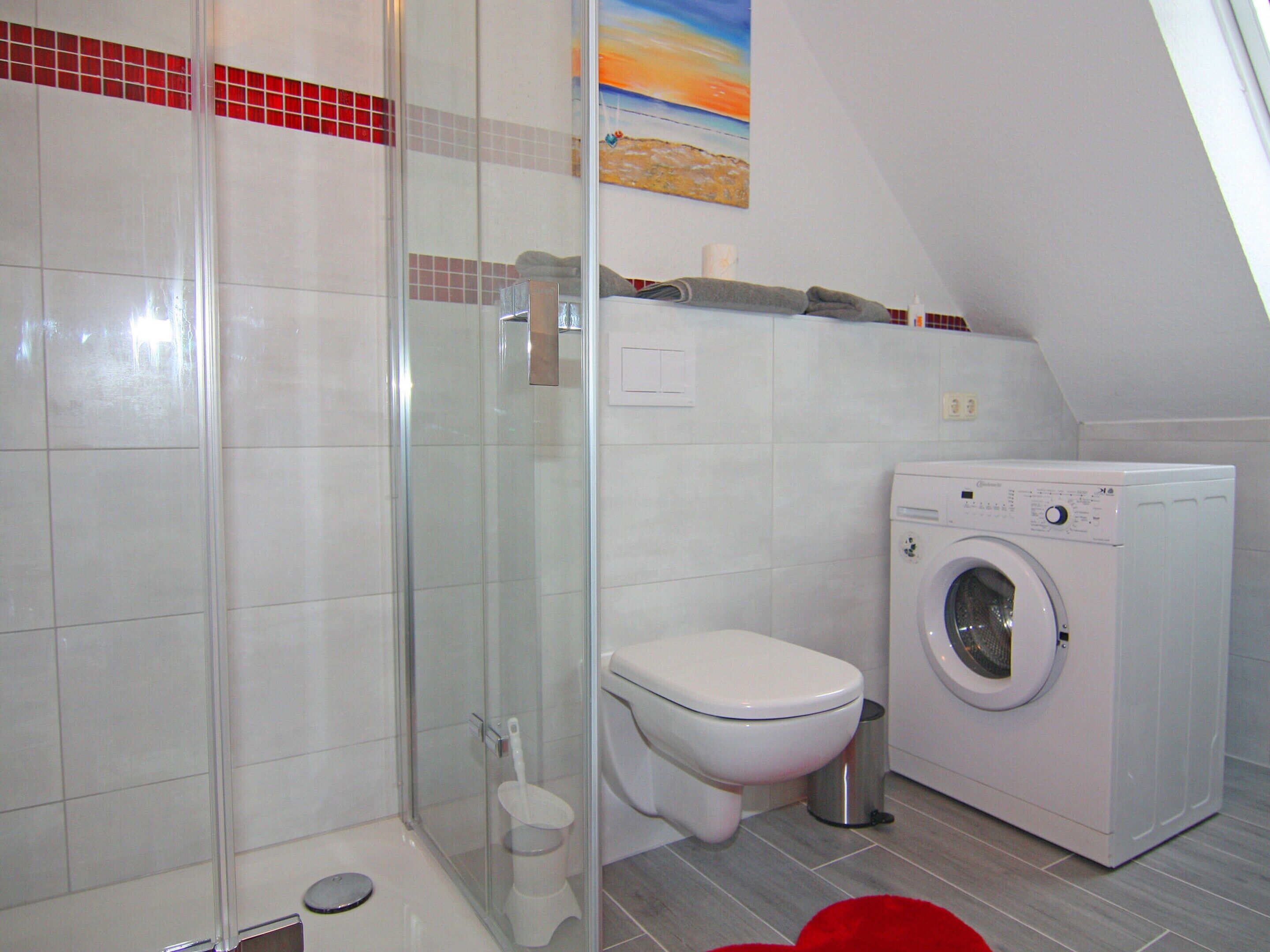 A bathroom with a glass shower enclosure, a toilet, and a front-loading washing machine.