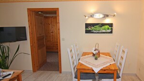 Un comedor con una mesa de madera, sillas blancas, un televisor montado en la pared y un elemento decorativo en la pared.