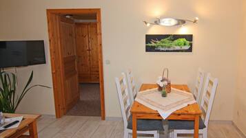 A dining area with a wooden table, white chairs, a TV mounted on the wall, and a decorative wall piece.