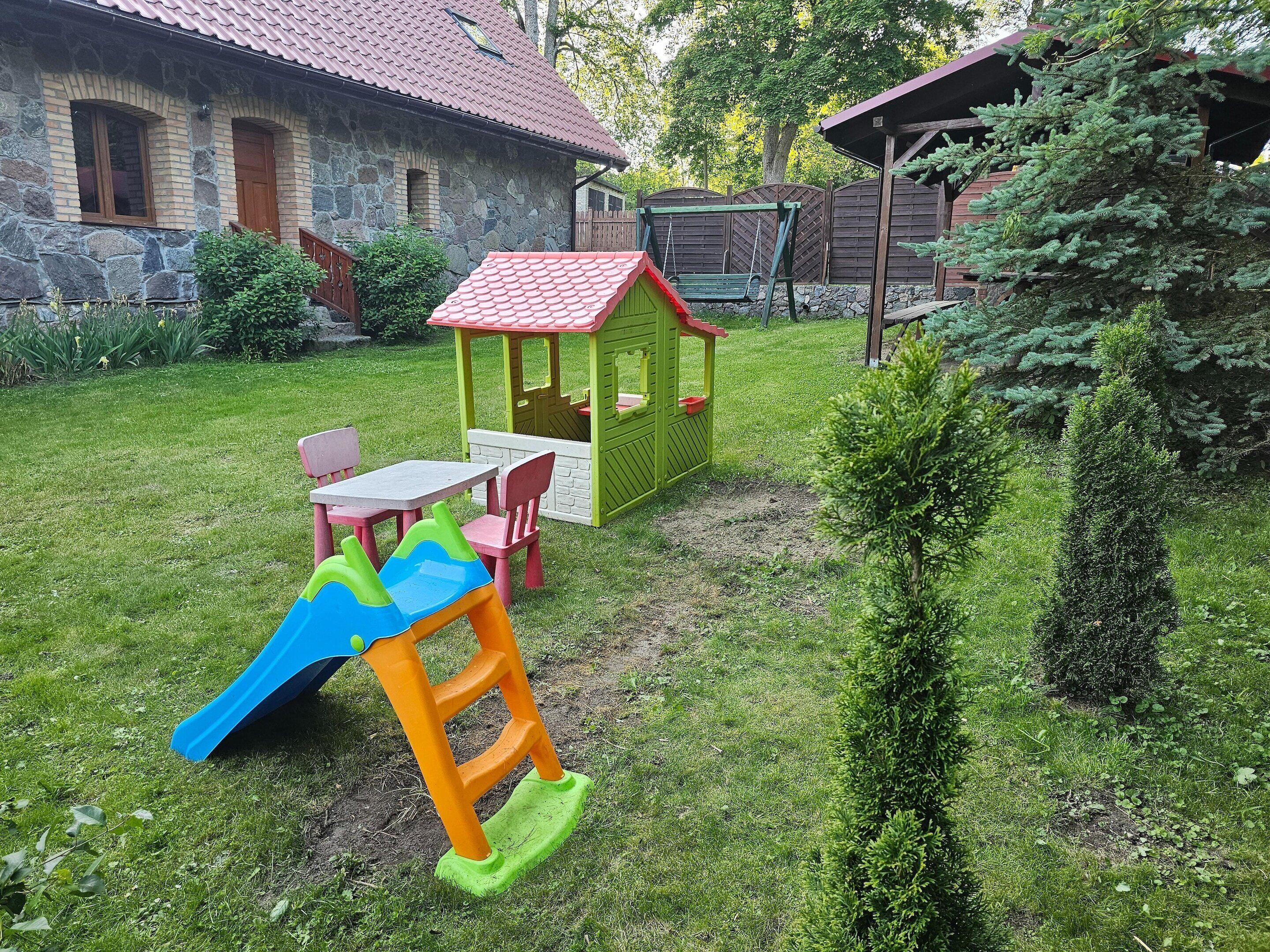 A backyard with a playhouse, a slide, and a small table with chairs.