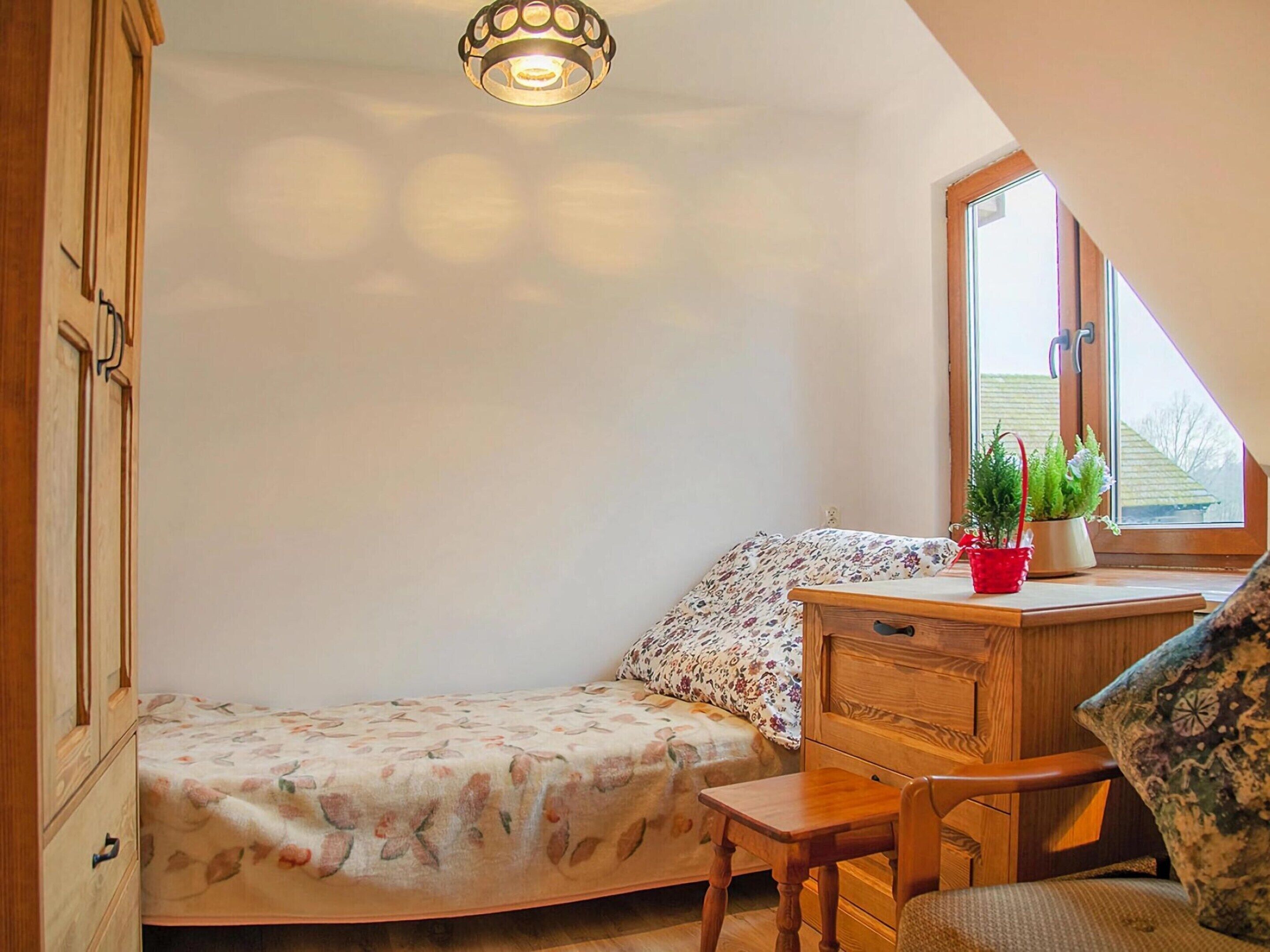 A bedroom with a bed, a wooden desk, a chair, a window, and a ceiling light.