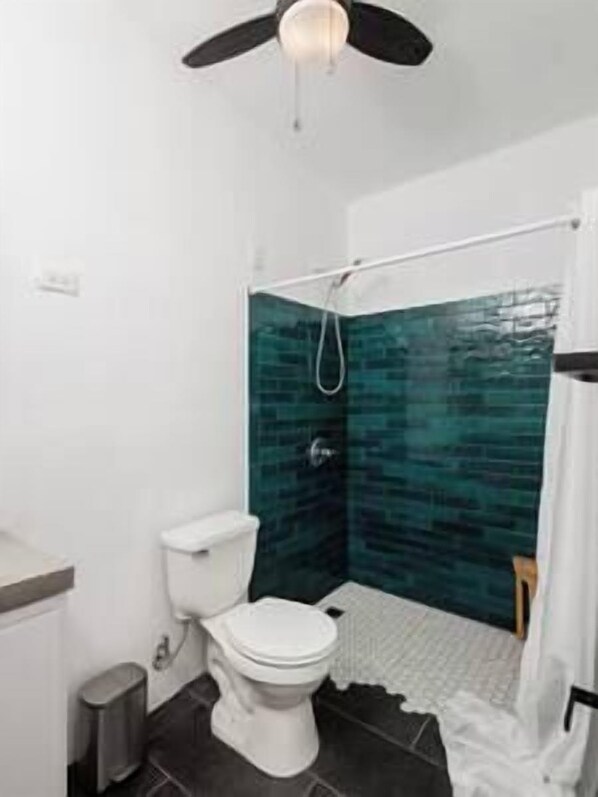 A bathroom with a white toilet, a shower with a glass door, and a ceiling fan. - Casa Mariposa - Hilltop home with Pool and Rooftop (Puerto Diablo)