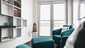 Een moderne woonkamer met smaragdgroene fauteuils, een witte boekenkast en een groot raam.