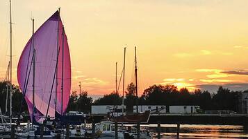 A marina with sailboats docked at wooden piers, calm water reflecting the sunset.