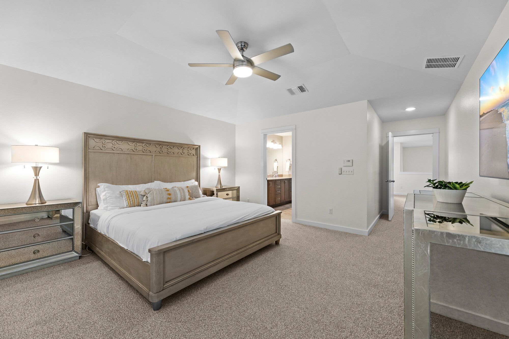 A bedroom with a bed, bedside tables, a ceiling fan, and a view of the bathroom.