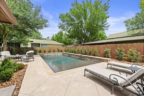 A backyard with a swimming pool, lounge chairs, and a wooden fence. - Large South Austin Home with a Pool (Austin)