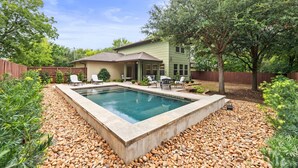 A house with a swimming pool surrounded by pebbles, a patio with chairs, and a wooden fence. - Large South Austin Home with a Pool (Austin)