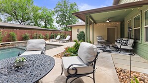 A covered patio with a pool, outdoor seating, and a view of the backyard. - Large South Austin Home with a Pool (Austin)