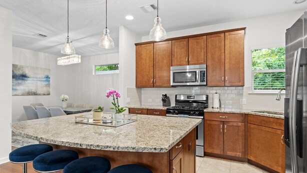 A modern kitchen with granite countertops, stainless steel appliances, wooden cabinets, and pendant lighting. - Large South Austin Home with a Pool (Austin)