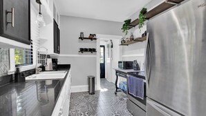 Una cocina moderna con un refrigerador de acero inoxidable, un microondas y una cafetera. Hay estantes con plantas y utensilios de cocina.